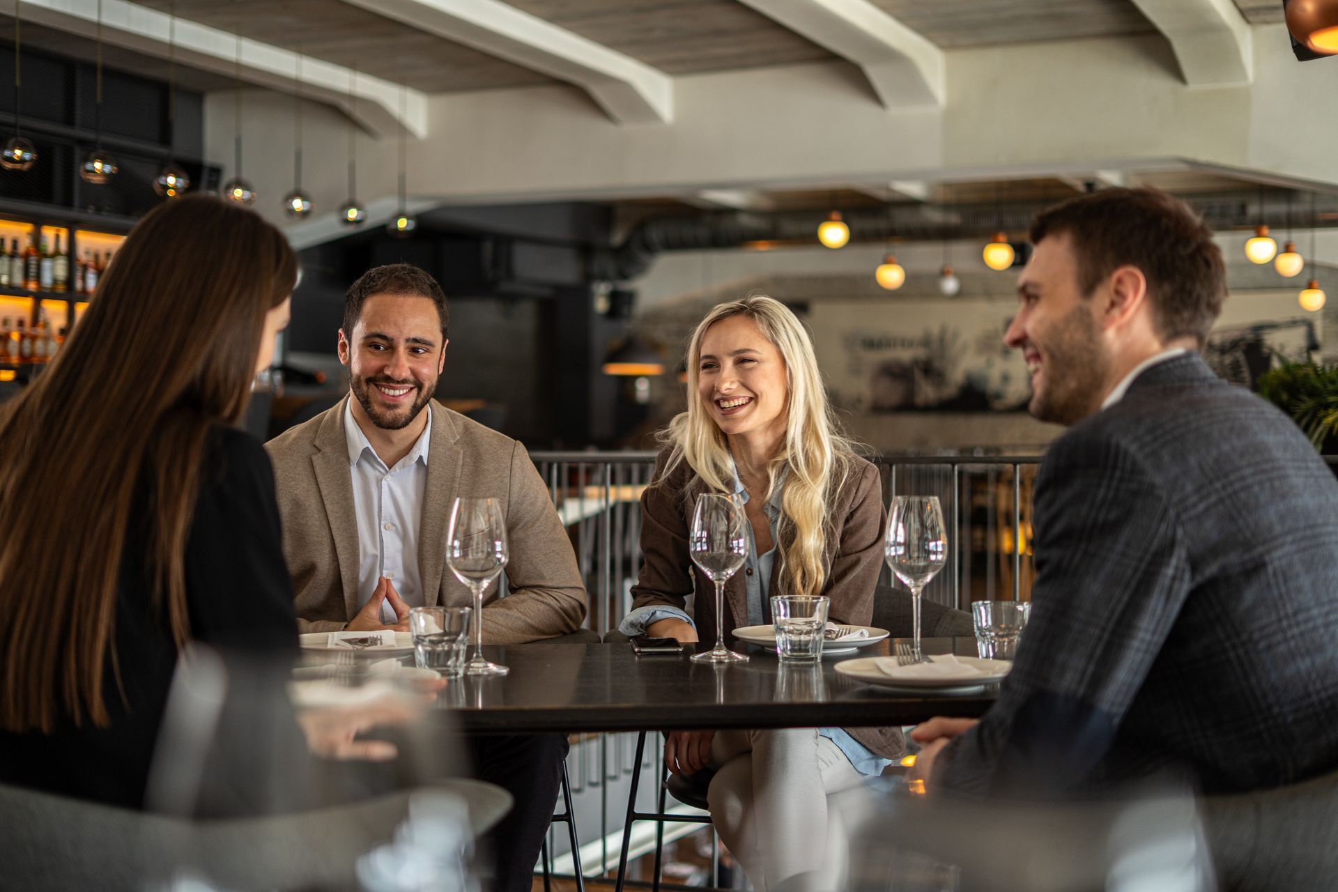 Quatre personnes rient à une table de restaurant, avec des verres et de la nourriture.