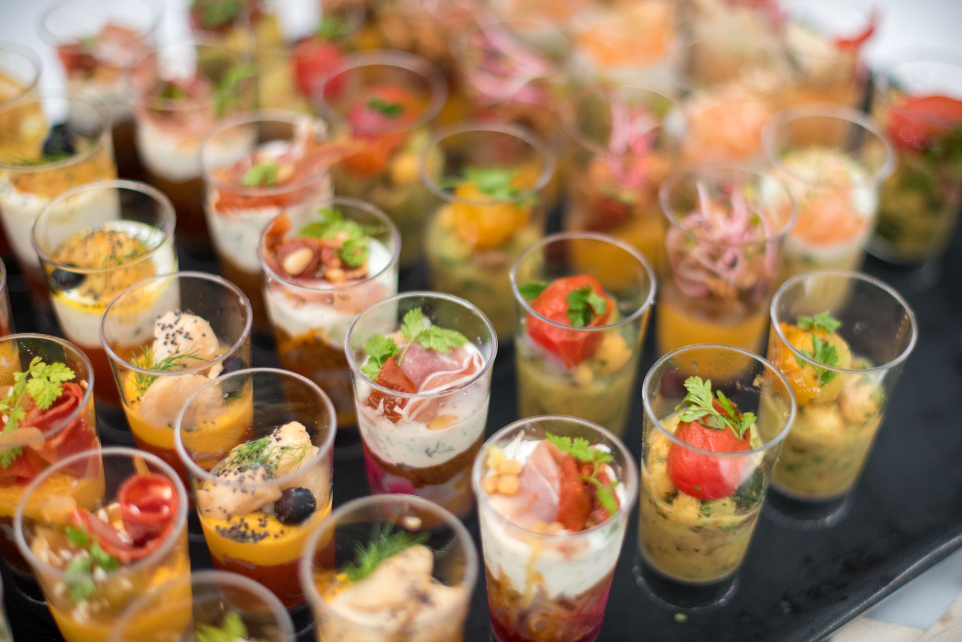 Plateau d'amuse-gueules assortis dans de petits gobelets transparents, de couleurs et de textures variées.