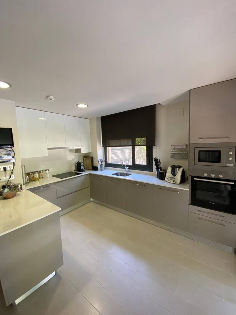 Cocina moderna en blanco y gris con encimeras en forma de L, horno empotrado y ventana sobre el fregadero.