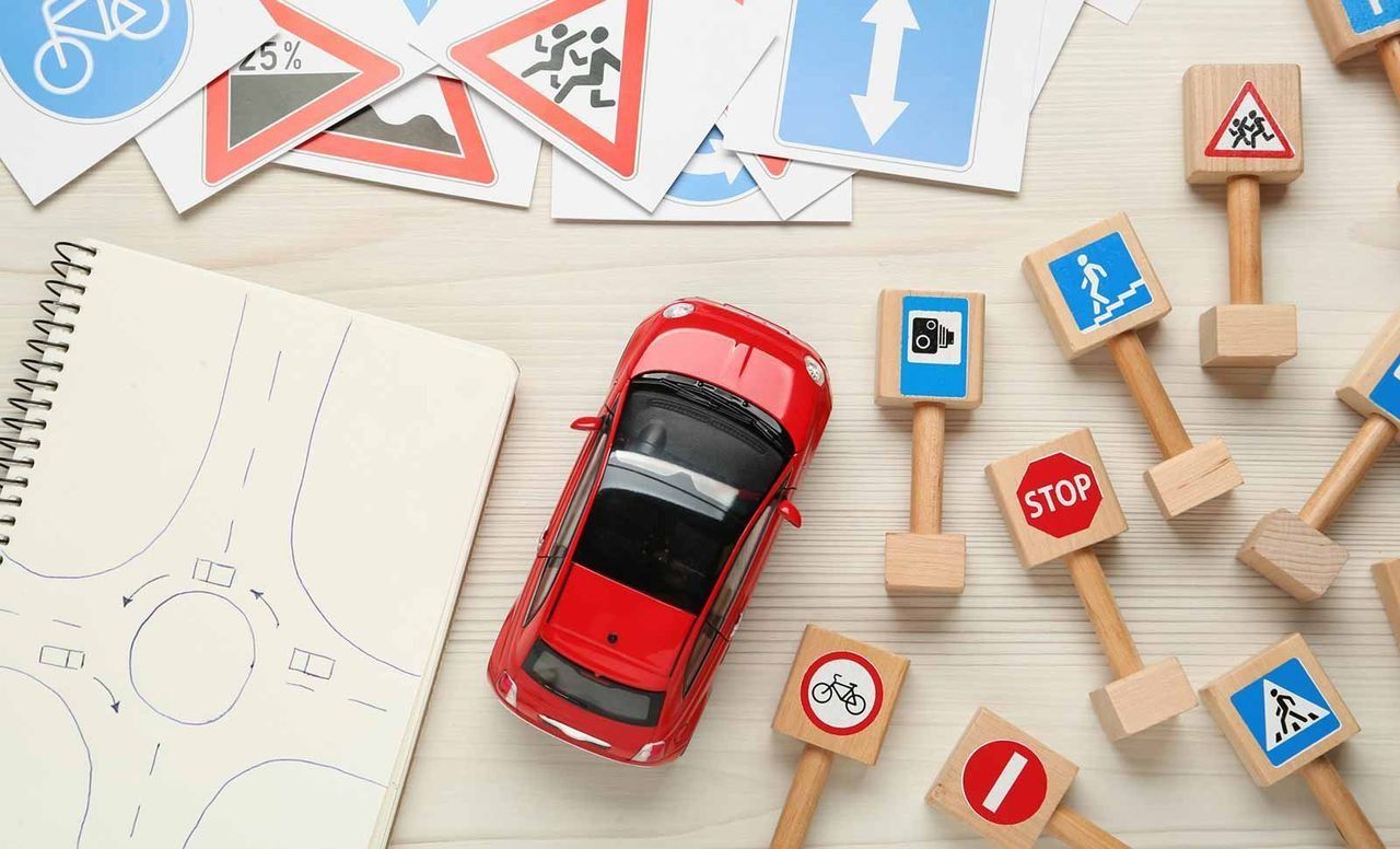 Un coche de juguete está rodeado de señales de tráfico de madera y un cuaderno.