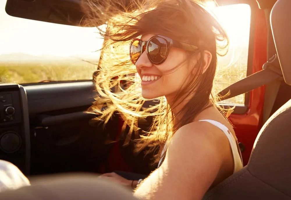 Una mujer que lleva gafas de sol está sentada en un coche con su cabello ondeando al viento.