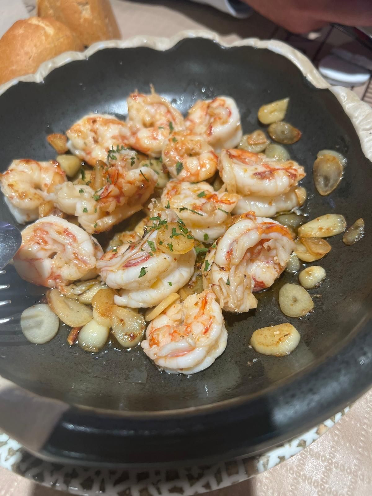 Un plato negro cubierto con camarones y ajo sobre una mesa.