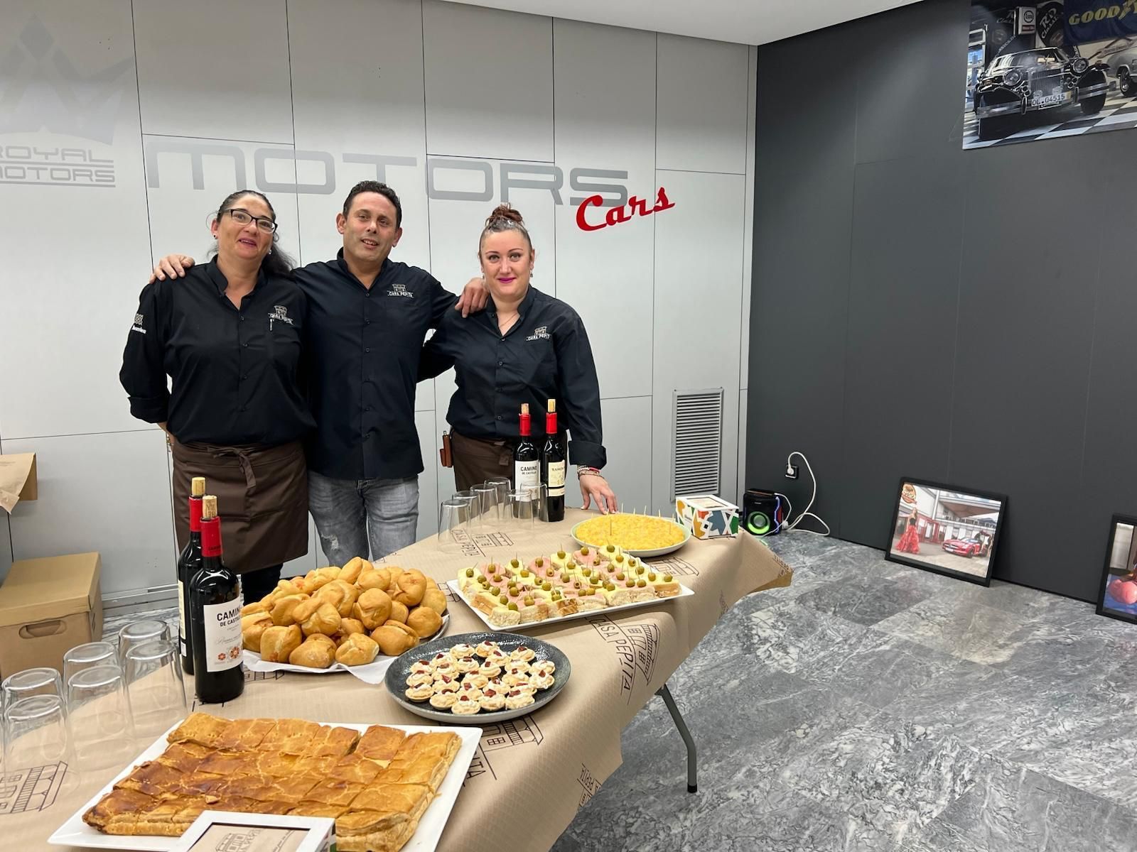 Un grupo de personas de pie alrededor de una mesa con comida y vino.