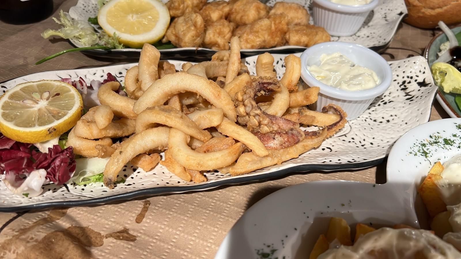 Un plato de comida con patatas fritas, calamares y limón sobre una mesa.