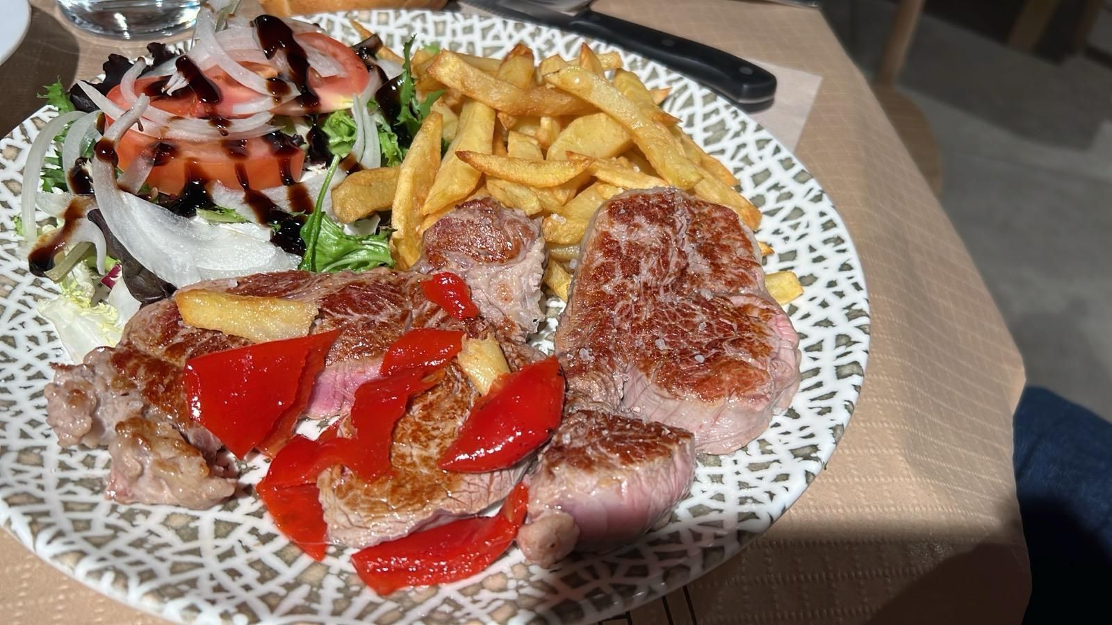 Un plato de comida con carne y patatas fritas en una mesa.