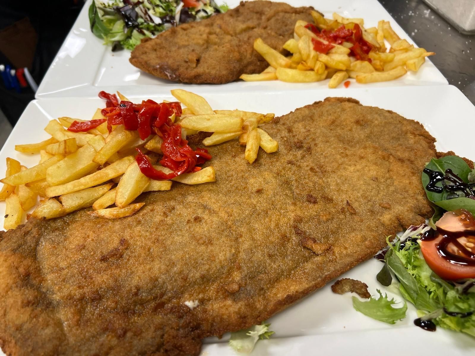 Un plato de comida con patatas fritas y una ensalada en una mesa.