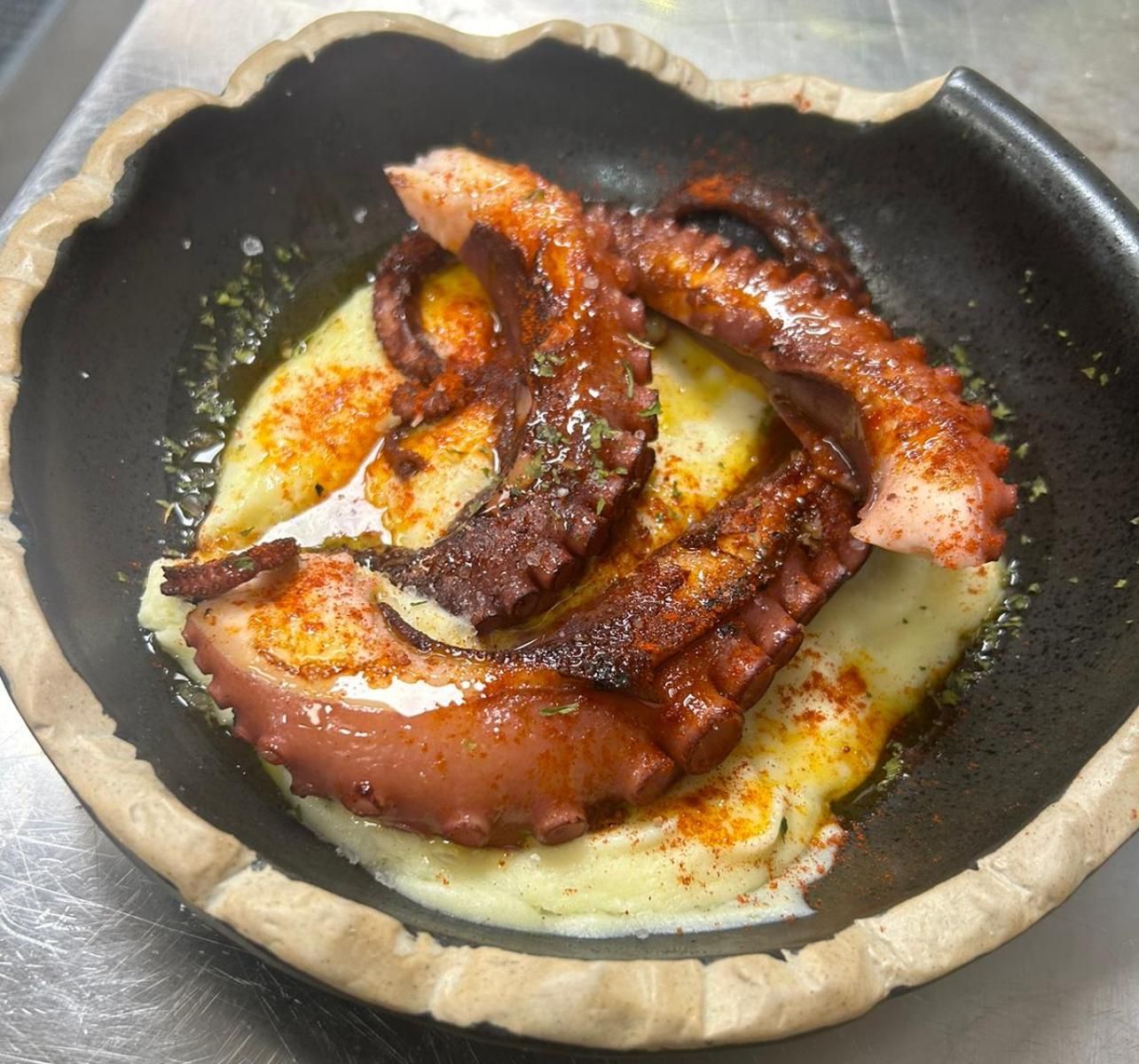 Un tazón de comida con un pulpo encima de puré de papas.