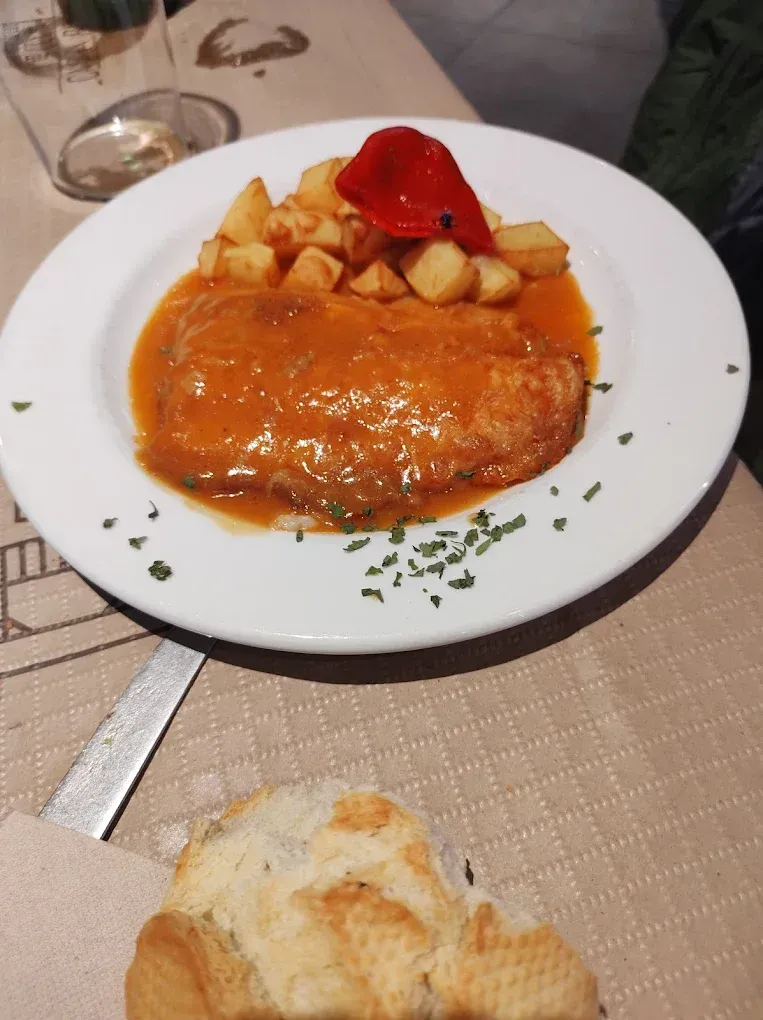Un plato blanco cubierto con carne y patatas sobre una mesa.