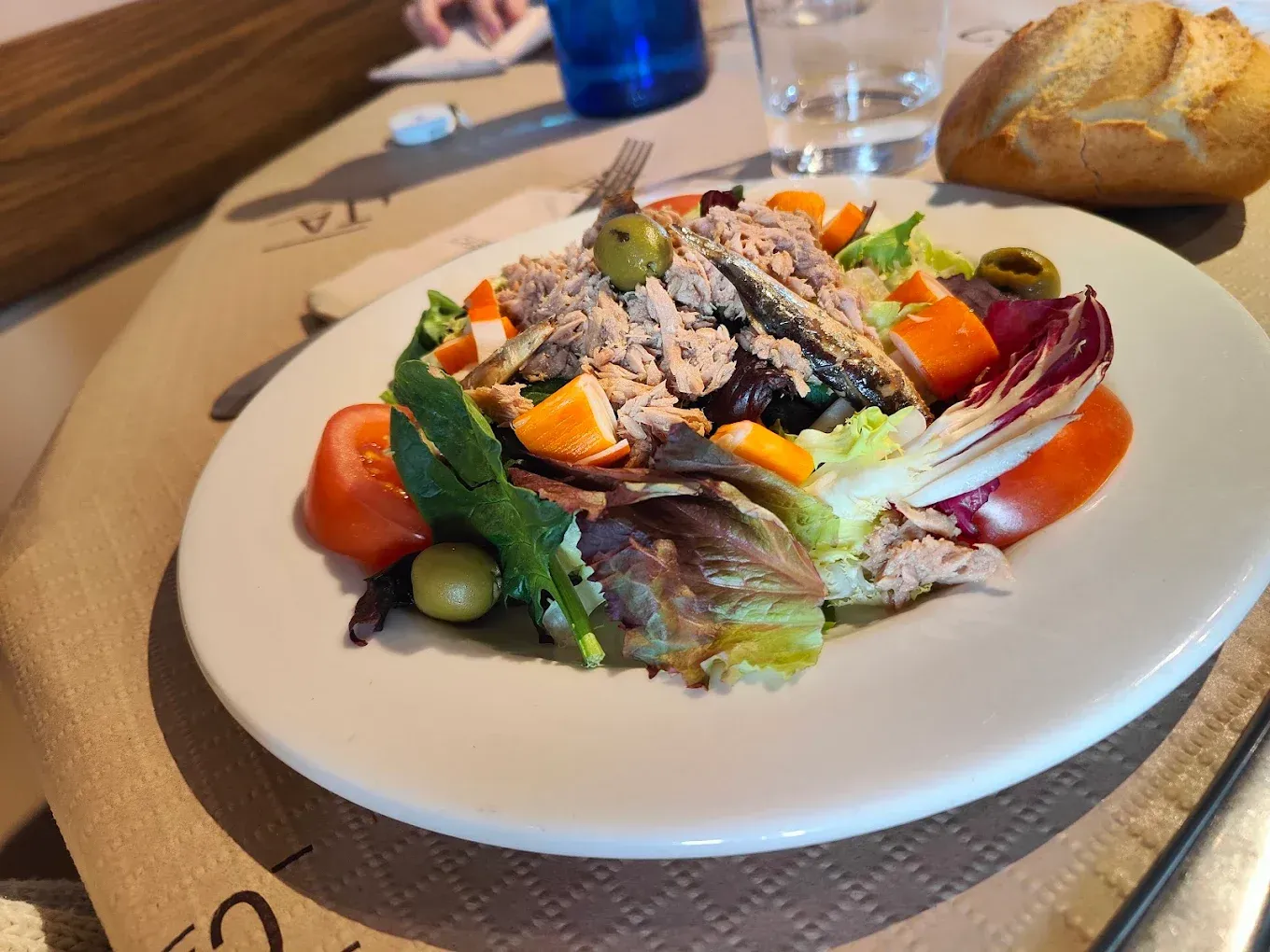 Una ensalada con atún, tomates y aceitunas en un plato blanco.