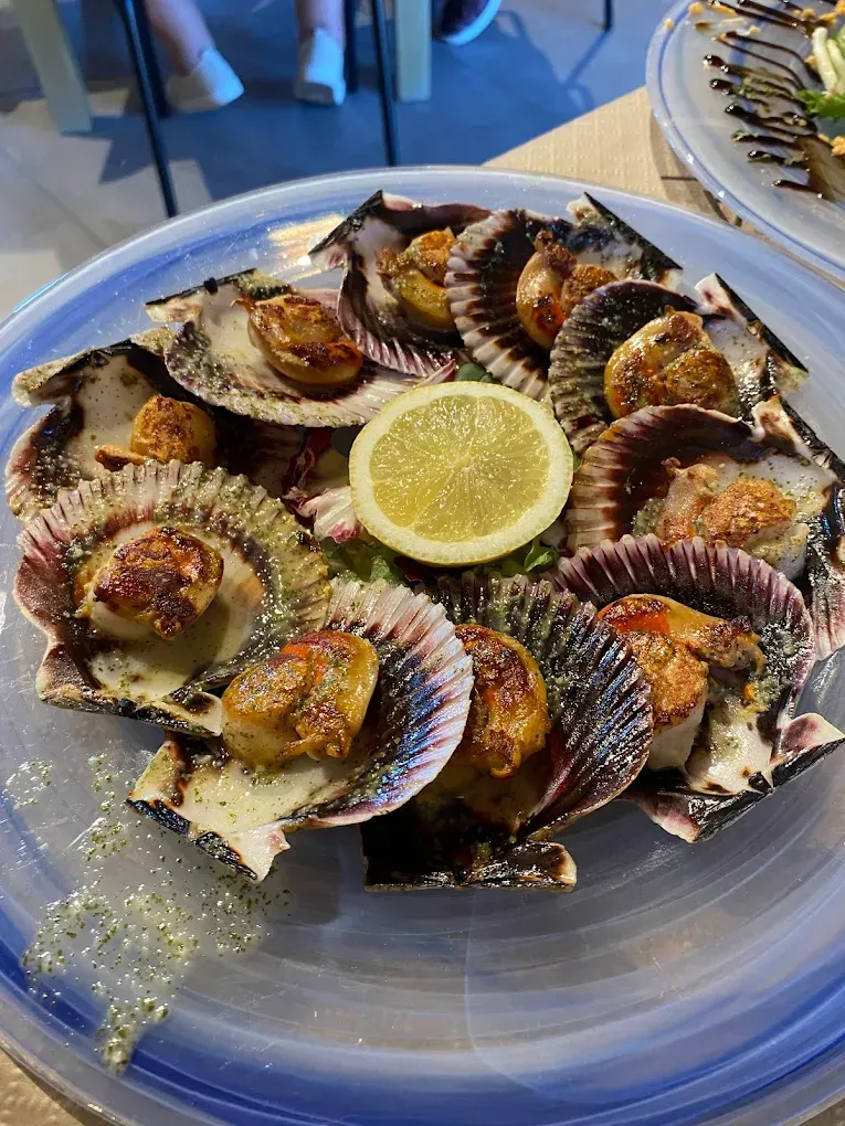 Un plato azul cubierto con vieiras y una rodaja de limón.