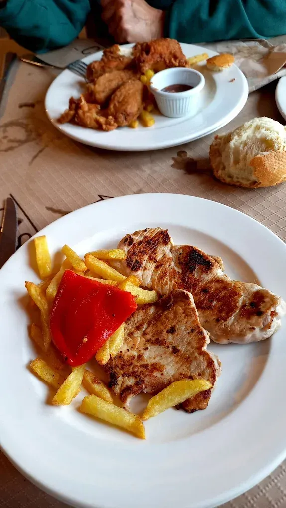 Un plato blanco cubierto con carne y papas fritas sobre una mesa.