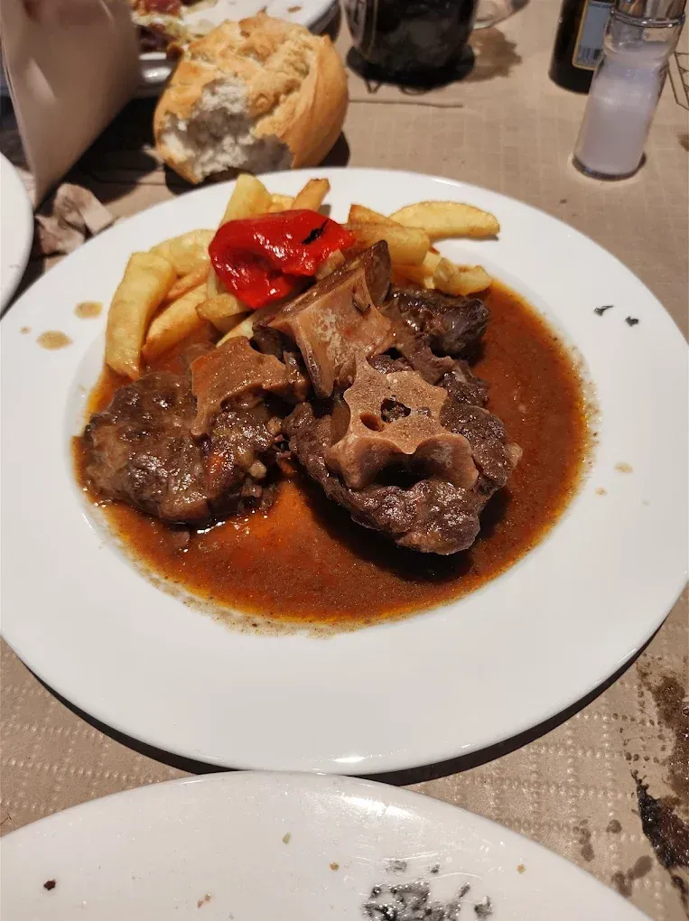Un plato blanco cubierto con carne y papas fritas.