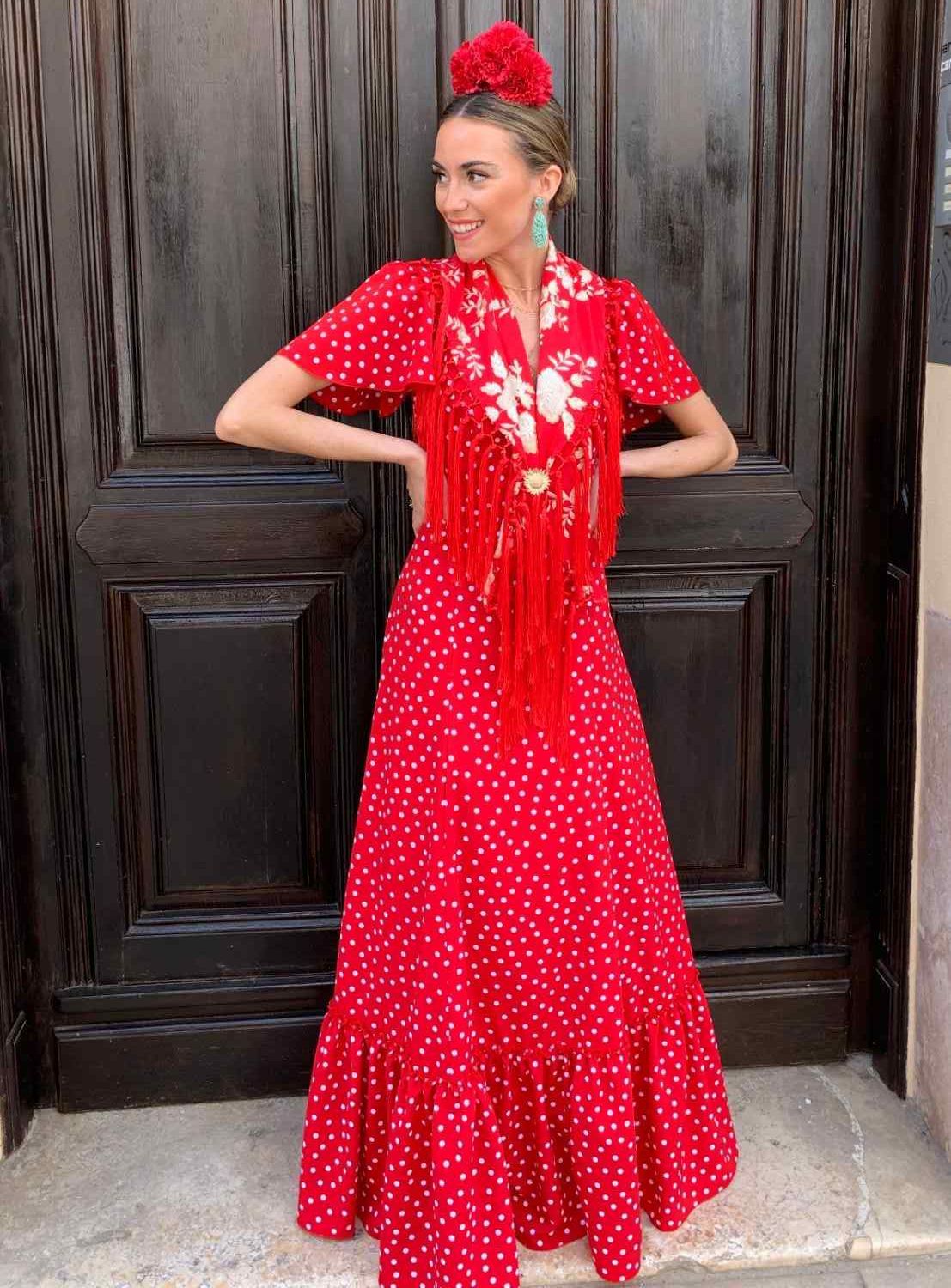 Mujer con un vestido rojo de lunares posando frente a una puerta de madera oscura, luciendo un tocado rojo a juego.