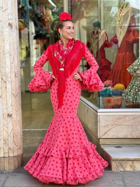 Mujer con un vestido de flamenco rosa brillante de pie junto al escaparate de una tienda.
