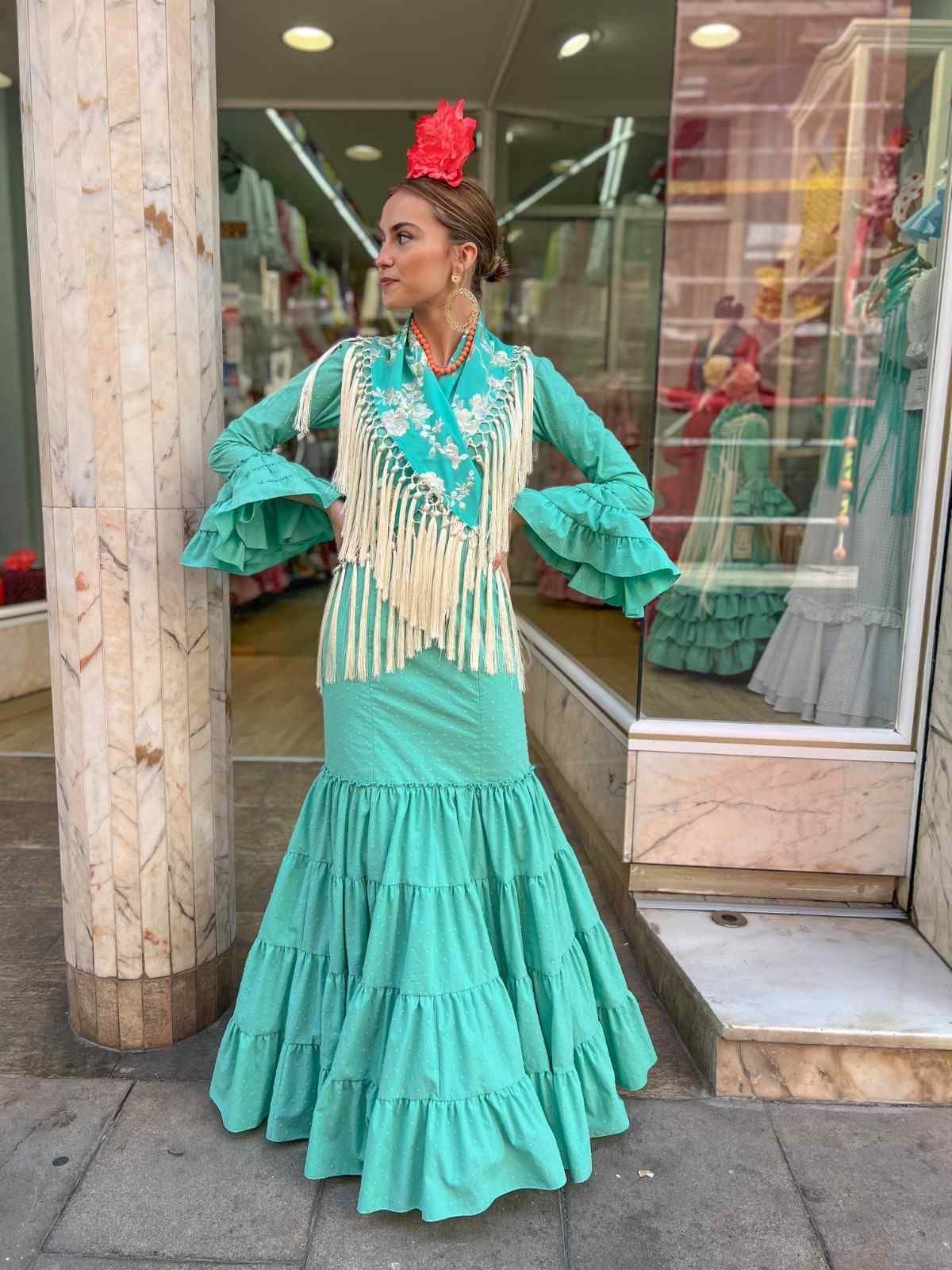 Una persona con un vestido flamenco turquesa posando frente a una tienda.