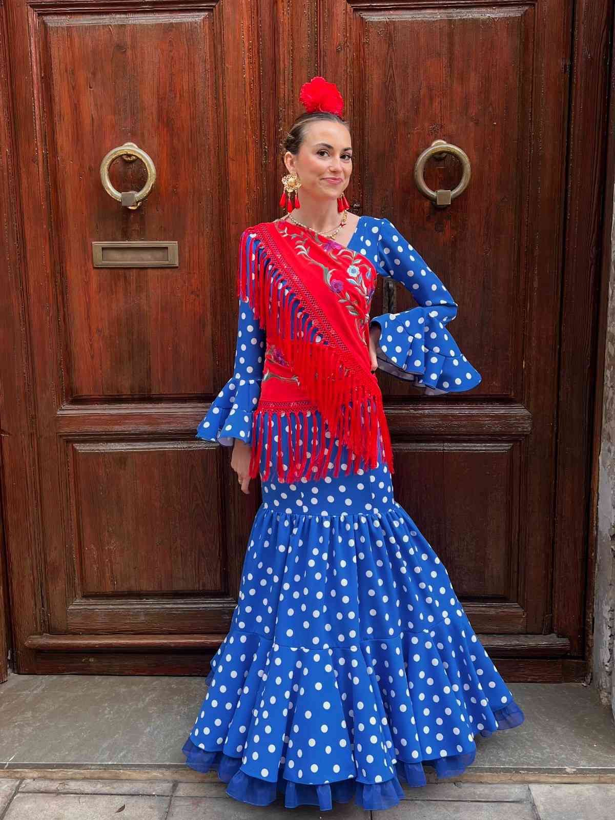 Mujer con un vestido flamenco azul de lunares posando frente a una puerta de madera.