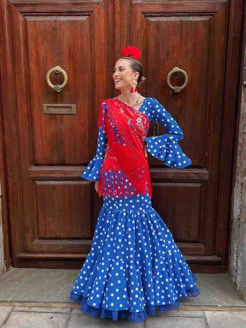 Mujer con un vestido de lunares rojos y azules posando frente a una puerta de madera.