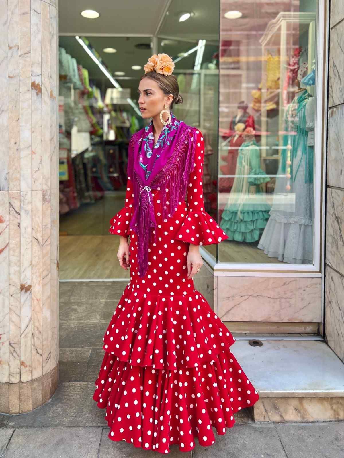 Mujer con un vestido de flamenco rojo de lunares de pie frente a una tienda.