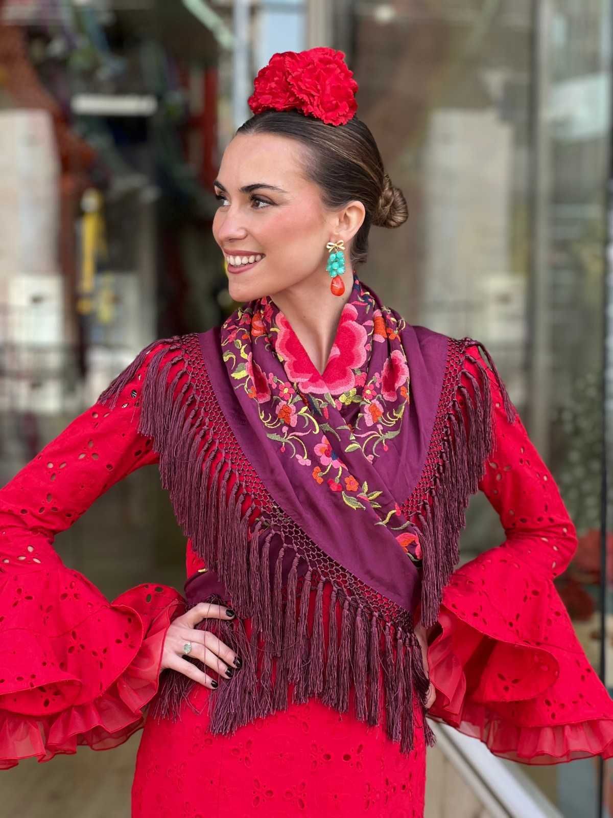 Mujer con un vestido flamenco rojo brillante y un chal con flecos, de pie y sonriendo al aire libre.