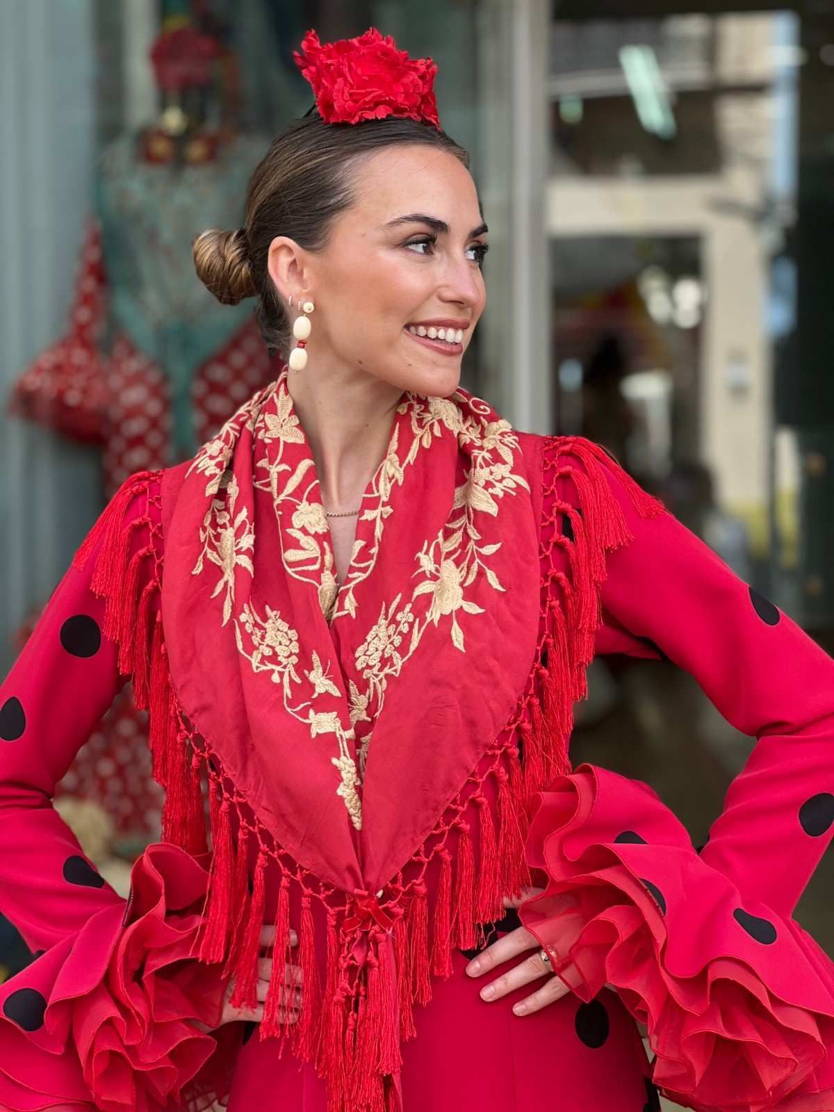 Mujer con un vestido de flamenco rojo y un chal a juego, sonriendo con las manos en las caderas al aire libre.