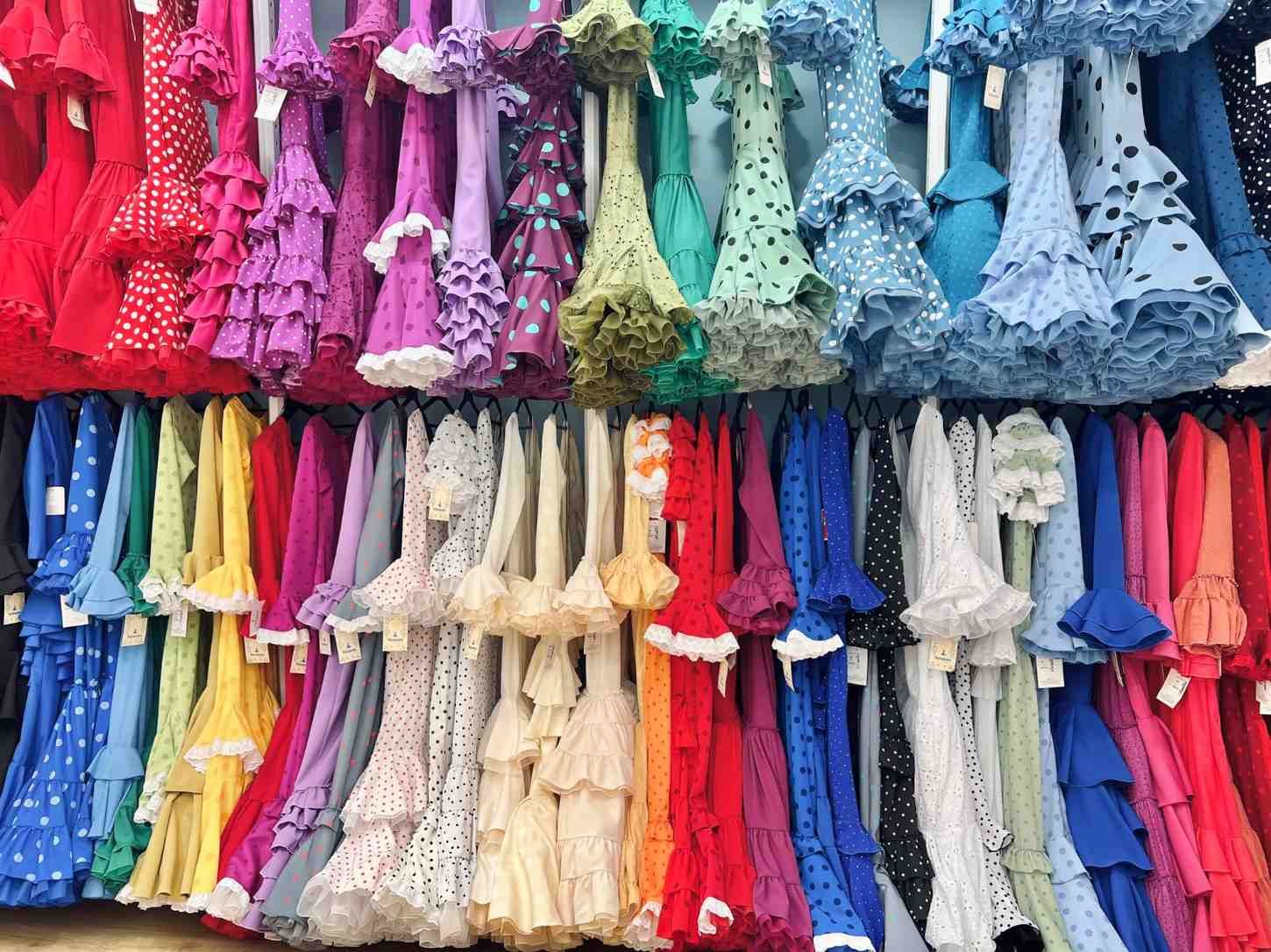 Filas de vestidos coloridos colgados en percheros en una tienda de ropa.