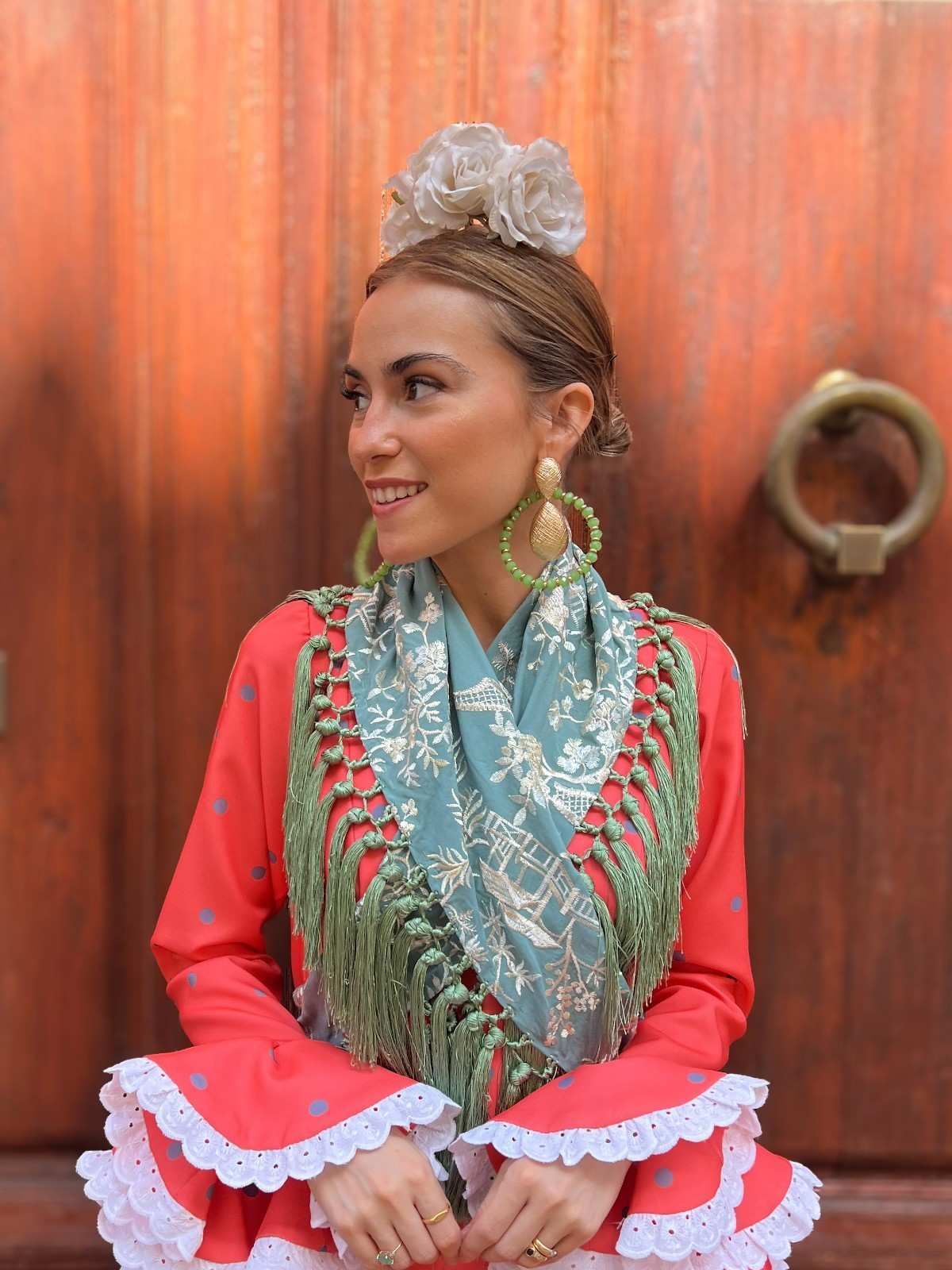 Persona vestida con un atuendo bordado en rojo y menta, sonriendo frente a una pared de madera.