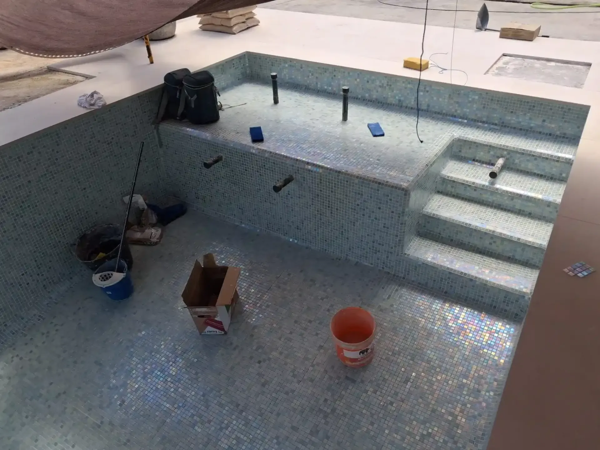 Dos trabajadores reparando una piscina junto a una casa de piedra y un patio