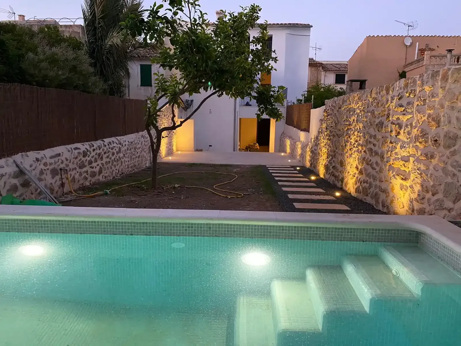 Tres personas inspeccionan una piscina junto a una casa blanca moderna con grandes puertas de cristal.