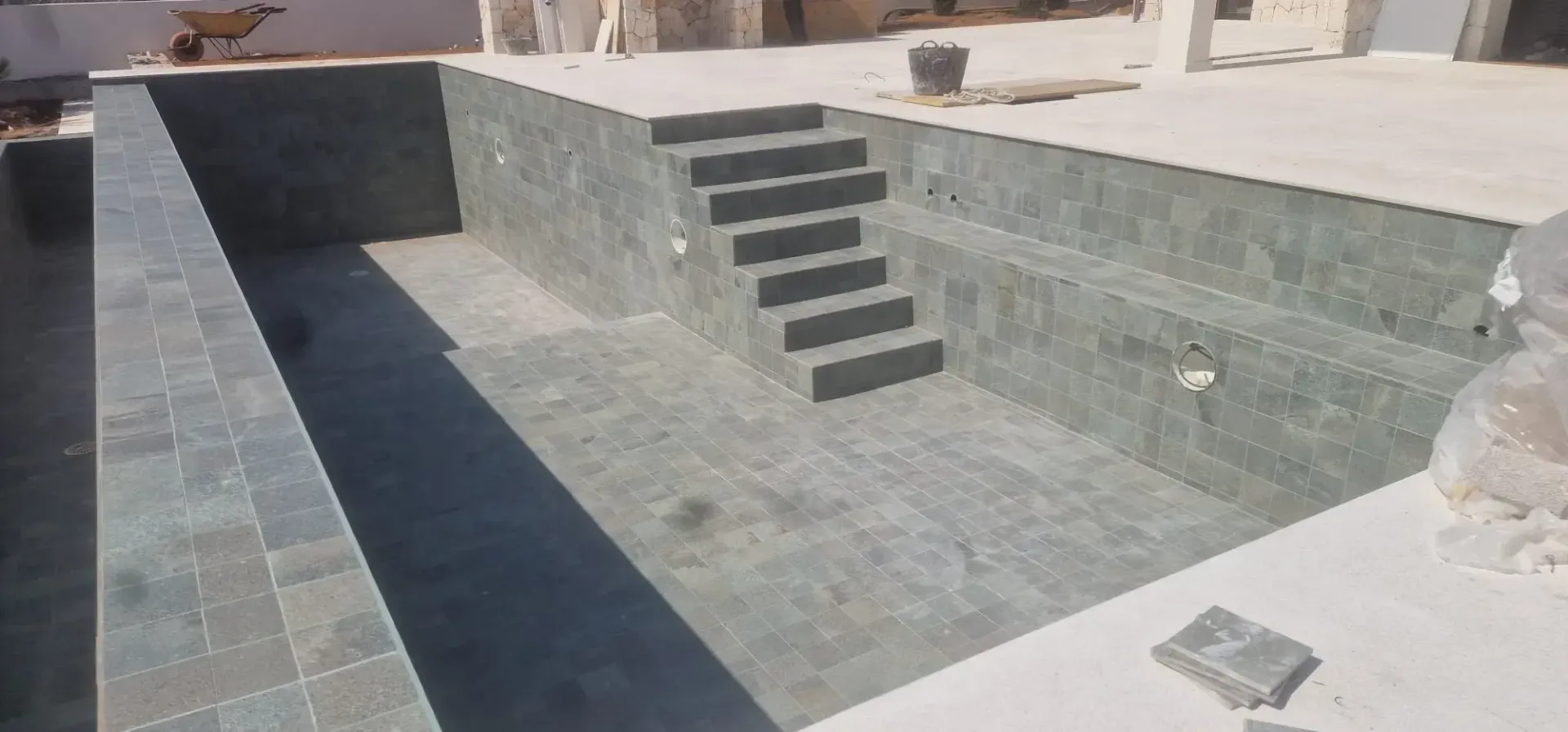 Tres obreros con cascos revisan unos planos frente a una casa de piedra en remodelación.