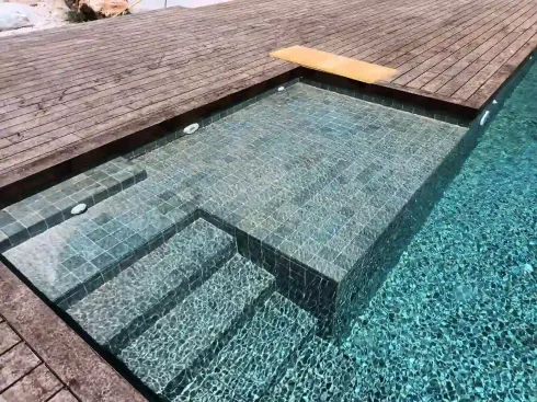Trabajadores haciendo tareas de mantenimiento en una piscina azul, junto a un patio de piedra y una palmera