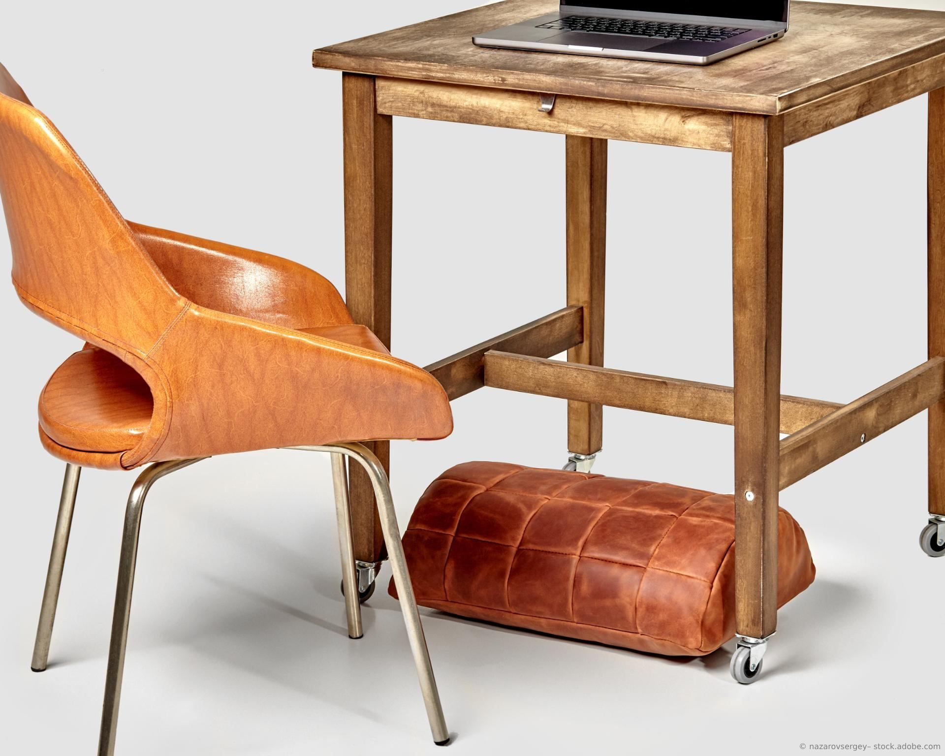 Ein Schreibtisch aus Holz mit einem Stuhl und Fußpolster