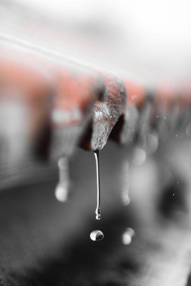 Gotas de lluvia que caen de una hilera de ganchos o accesorios borrosos en una escena con poca profundidad de campo.