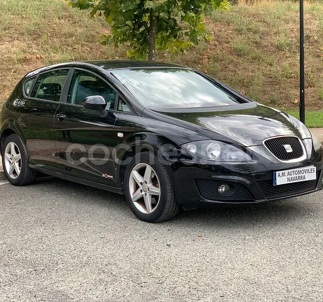 Un coche negro está estacionado en un estacionamiento al lado de un árbol.