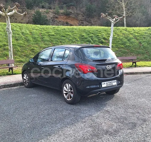 Un coche negro está aparcado en un estacionamiento al lado de una colina cubierta de hierba.