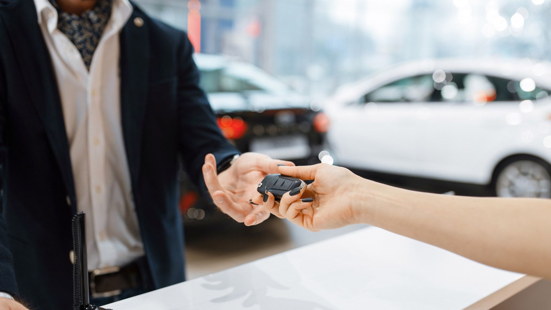 Un hombre le entrega una llave de coche a una mujer en un concesionario de automóviles.