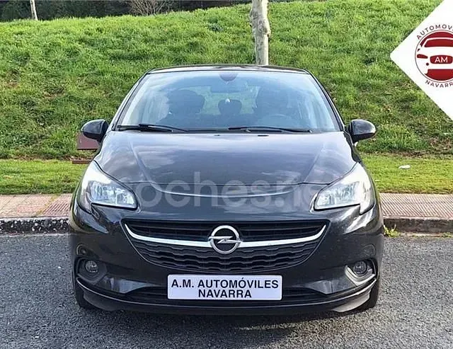Un coche negro está estacionado al costado de la carretera frente a una colina cubierta de hierba.