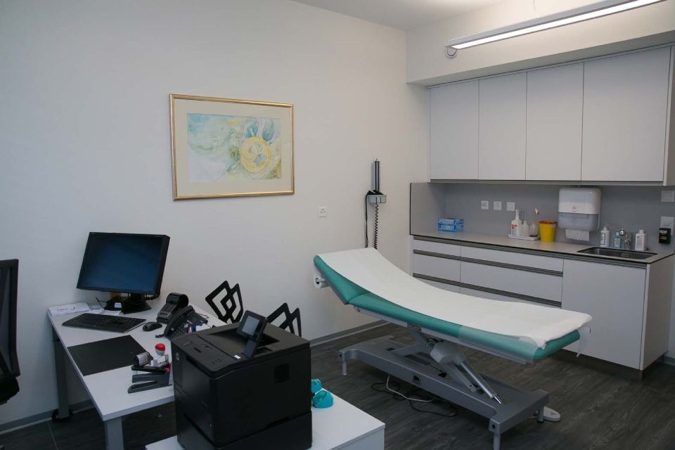 Un cabinet médical avec un canapé, un bureau, un ordinateur et une imprimante.