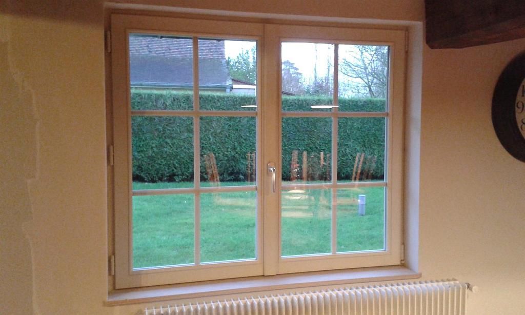 Une fenêtre d'une maison en bois donannt sur un jardin.