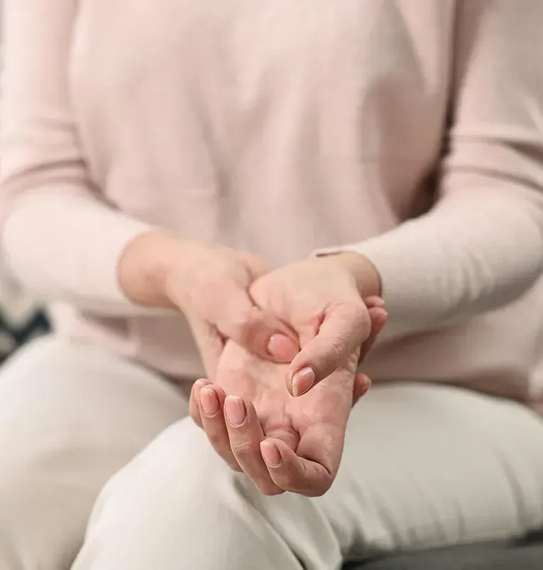 Una mujer está sentada en un sofá sosteniendo sus manos juntas.