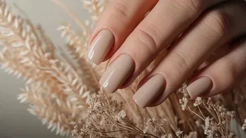 Las manos de una mujer con uñas largas sostienen un ramo de flores secas.