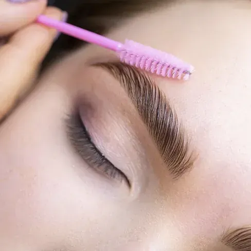 Una mujer se está depilando las cejas con un cepillo rosa.