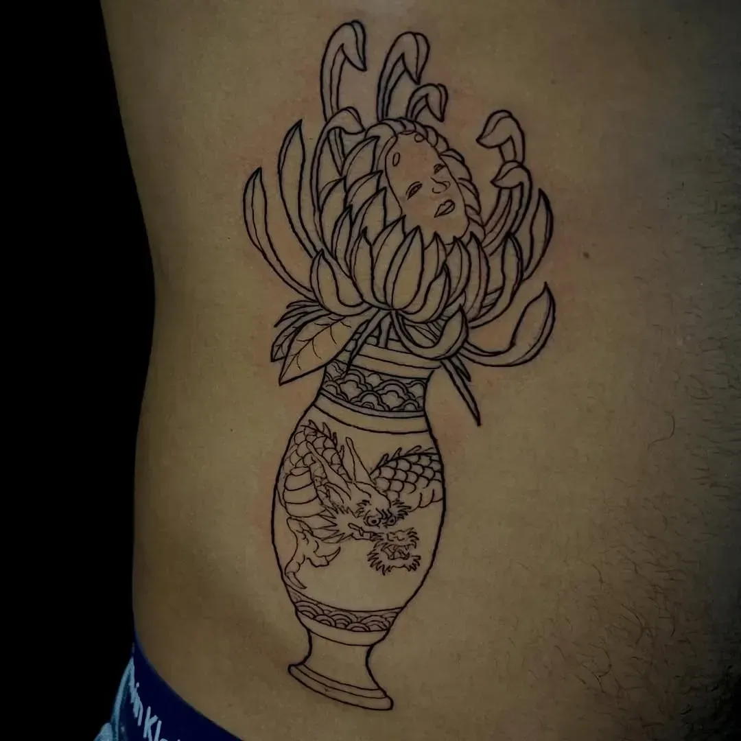 Tatuaje de contorno de un jarrón con un diseño de dragón y una flor que brota de él en el costado de una persona.