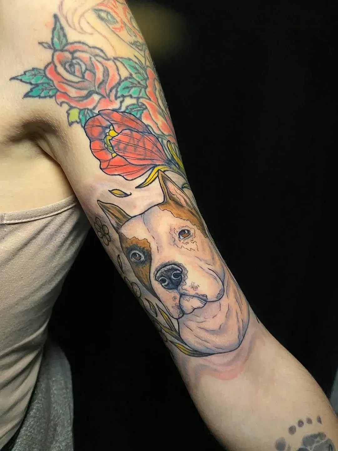 Tatuaje de la cara de un perro en el brazo de una mujer, rodeado de rosas de colores.