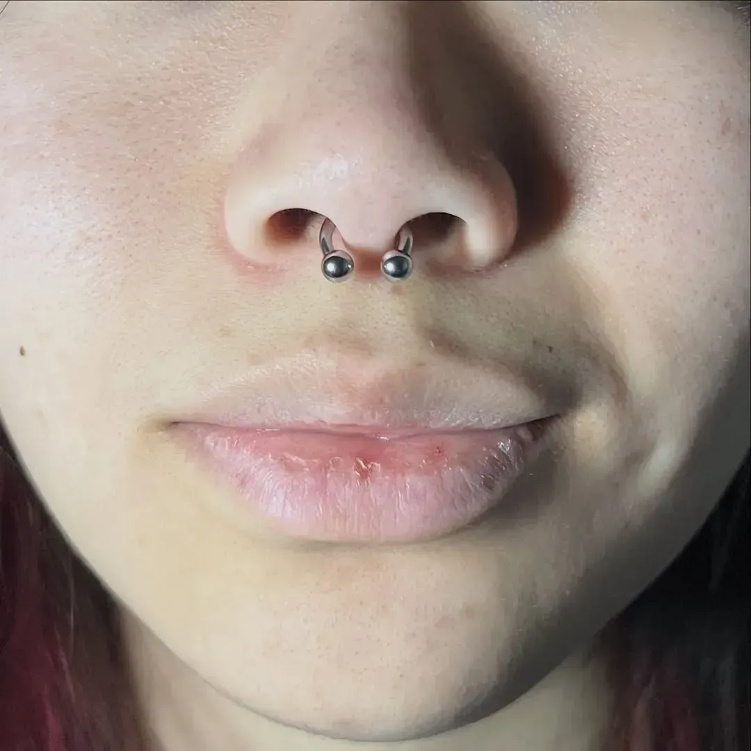 Primer plano del rostro de una persona con un piercing en el tabique nasal. La boca está cerrada y la piel es clara.