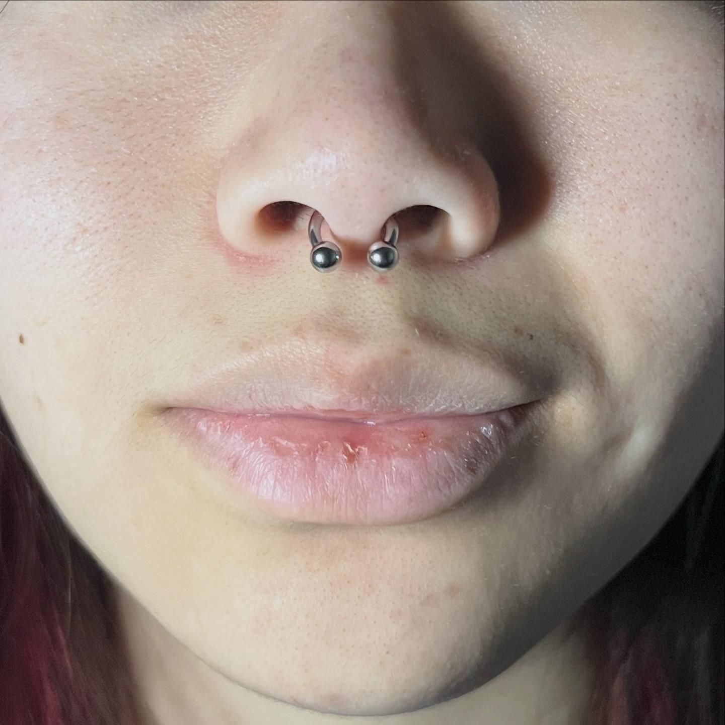 Primer plano del rostro de una persona con un piercing en el tabique nasal. 