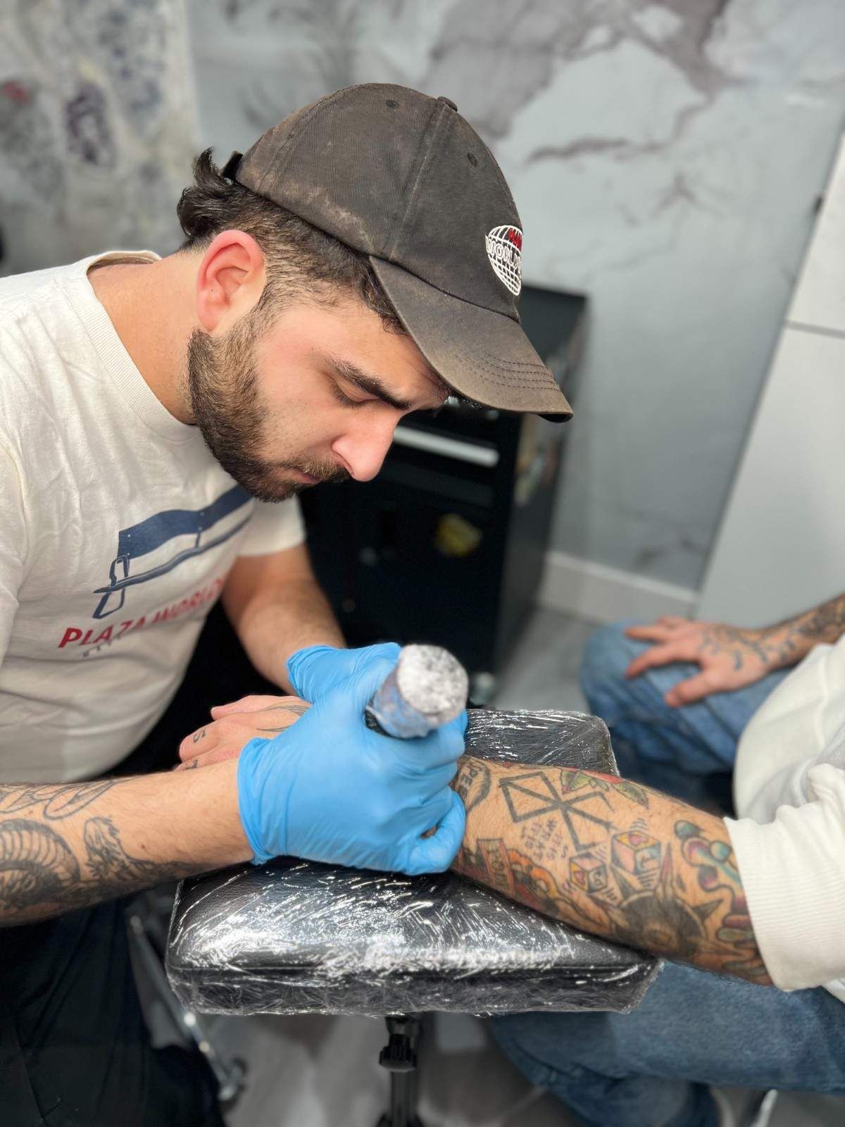 Hombre con sudadera y gorra gris de Roca Wear, se sitúa frente a una pared de mármol.