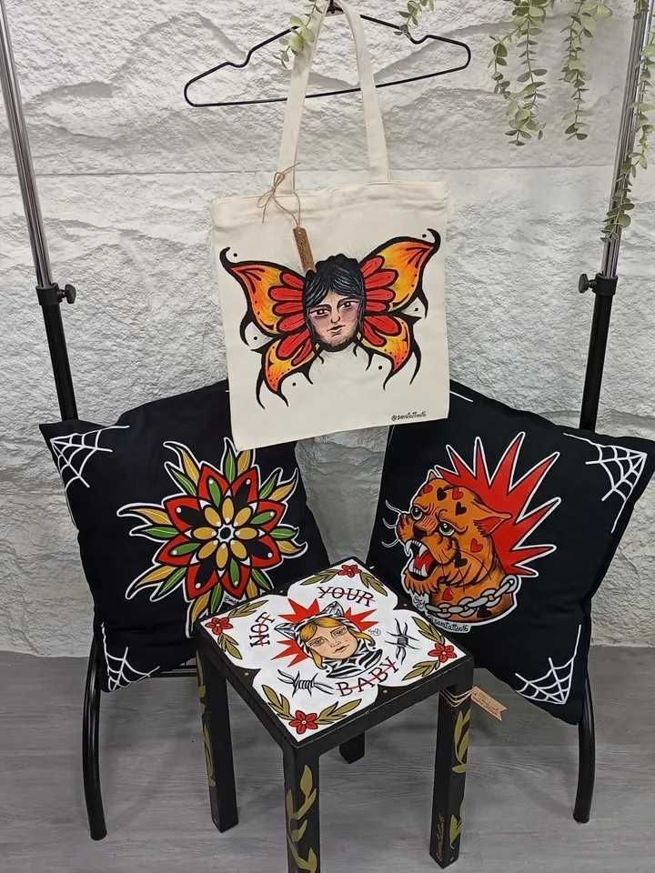 Bolso de mano y cojines con ilustraciones de estilo tatuaje. Una mesita con ilustraciones a juego y un diseño de mariposa.