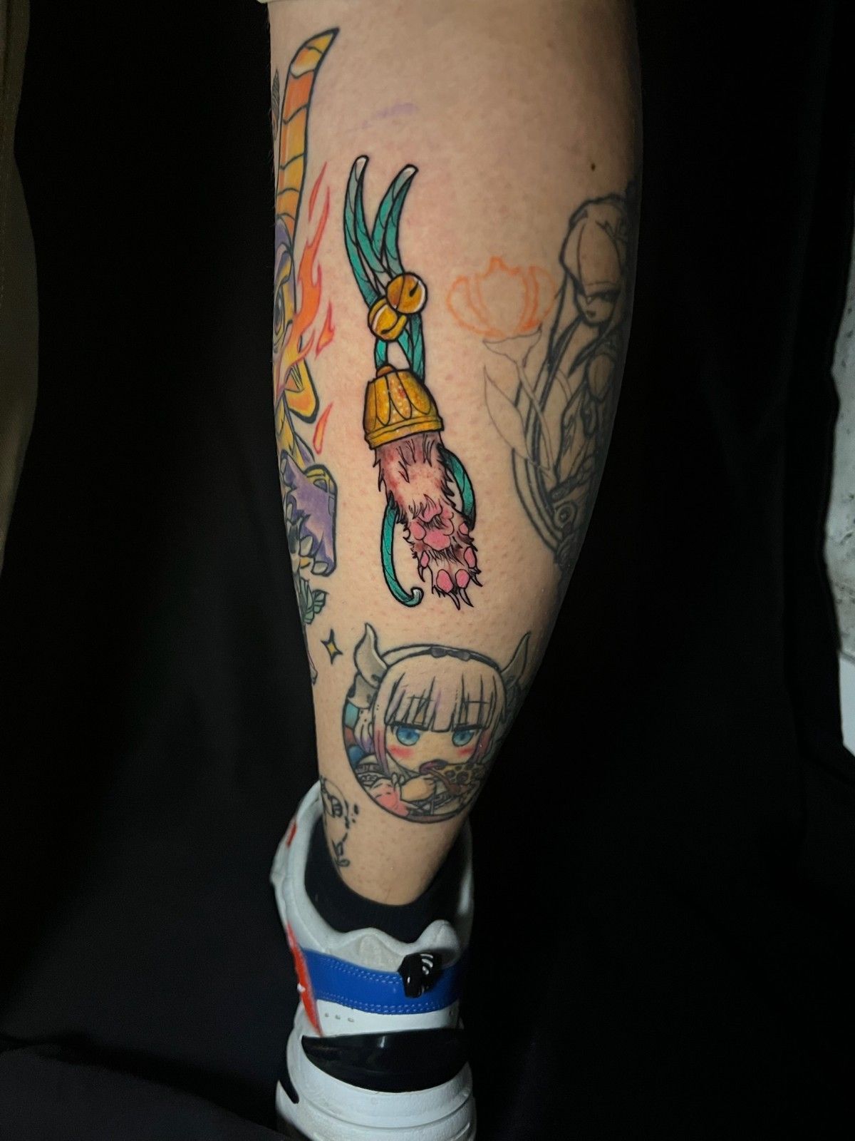 Pierna con tatuajes de dibujos animados coloridos, que incluyen una herramienta, una cara y otros diseños.