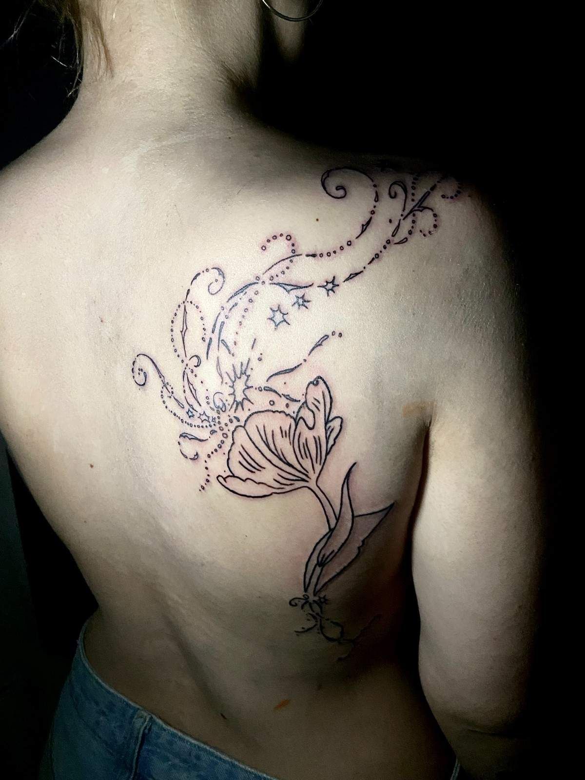 Tatuaje de un tulipán y un diseño en espiral en la espalda de una persona, cerca del hombro.