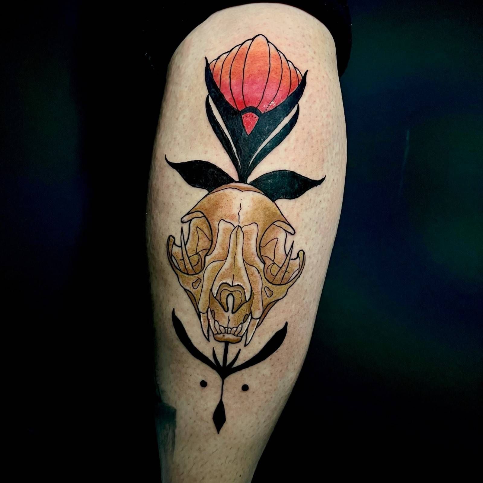 Tatuaje de una calavera de gato color canela con hojas negras, una flor de color rojo anaranjado 